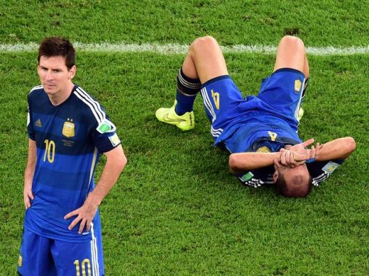 Argentina's Pablo Zabaleta lies on the pitch as Lionel Messi stands beside him after losing to Germany in the final, Rio de Janeiro, Brazil, July 13, 2014. (Francois Xavier Marit/AP via http://usatoday.com).